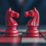 Investor placing chess pieces on a board shaped like a stock graph with bull and bear pieces, stocks, strategic market positioning. Copyright: KENZOGROW - stock.adobe.com