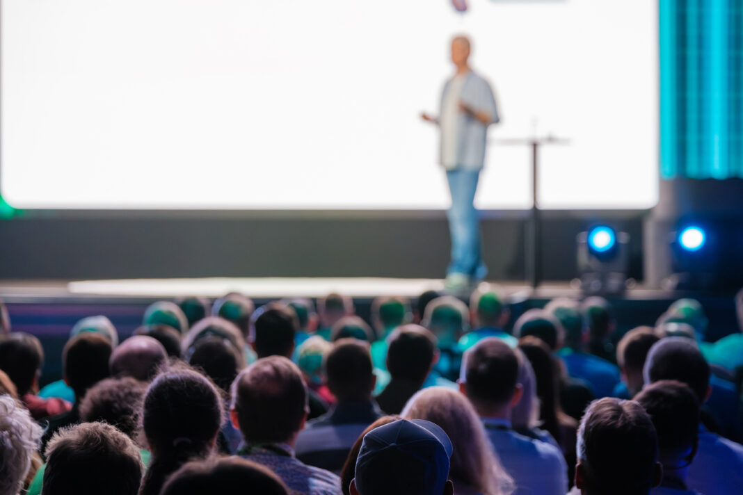 Symbolbild. Speaker delivering a presentation to a large audience at a business conference in a modern venue. Engaged attendees listen attentively. Copyright: Anton Gvozdikov - stock.adobe.com